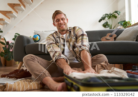 Image of young man, tourist struggling to push clothes inside full suitcase, packing for holiday 113329142