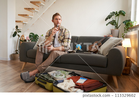 Portrait of young man packing for a trip, going on vacation, putting clothes inside suitcase, preparing for holiday Portrait of young man packing for a trip, going on vacation, putting clothes inside suitcase, preparing for holiday 113329602