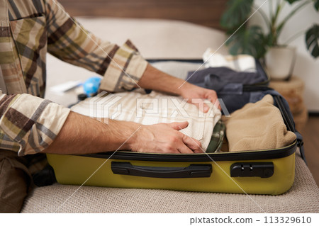 Male hands, tourist packing his clothes in luggage, putting items inside suitcase, getting ready for a vacation, going on holiday or business trip Male hands, tourist packing his clothes in luggage, putting items inside suitcase, getting ready for a vacation, going on holiday or business trip 113329610