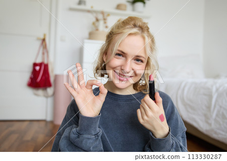 Portrait of young blond woman, content creator, recording video for social media about makeup, showing okay hand sign and lipstick, recommending good cosmetic product Portrait of young blond woman, content creator, recording video for social media about makeup, showing okay hand sign and lipstick, recommending good cosmetic product 113330287