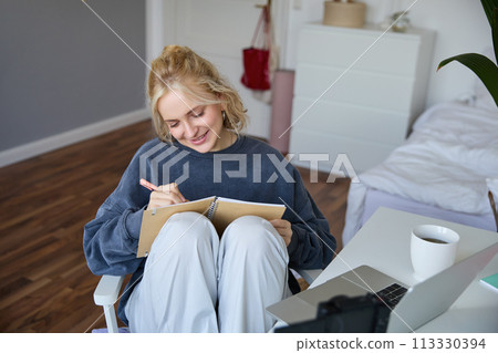 Portrait of smiling cute woman, lifestyle blogger, sits in her room with daily journal or planner, records video on digital camera, creates content for social media about daily routine Portrait of smiling cute woman, lifestyle blogger, sits in her room with daily journal or planner, records video on digital camera, creates content for social media about daily routine 113330394