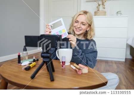 Portrait of beautiful smiling woman, recording video in her room, has camera on coffee table, reviewing makeup, doing lifestyle vlog for social media account, records a tutorial 113330555