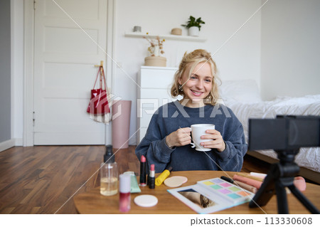Portrait of beautiful social media beauty blogger, sitting in front of digital camera on floor in bedroom, drinking tea and chatting, talking to followers Portrait of beautiful social media beauty blogger, sitting in front of digital camera on floor in bedroom, drinking tea and chatting, talking to followers 113330608
