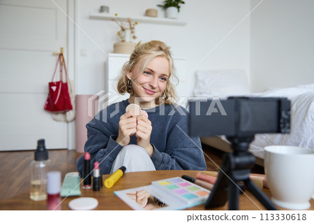 Portrait of beautiful and stylish young woman, vlogger recording video on her digital camera in a room, showing beauty products, making makeup tutorial for followers on social media Portrait of beautiful and stylish young woman, vlogger recording video on her digital camera in a room, showing beauty products, making makeup tutorial for followers on social media 113330618