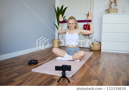 Portrait of young athletic woman recording home workout video, shooting content for sport fitness vlog, using resistance band and digital camera Portrait of young athletic woman recording home workout video, shooting content for sport fitness vlog, using resistance band and digital camera 113330638