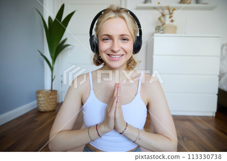 Wellbeing and people concept. Close up portrait of young woman in headphones, meditating, practice yoga, listens to podcast in earphones 113330738