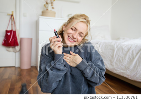 Portrait of young content creator, woman with social media account, recording video about makeup on digital camera, holding favorite lipstick, recommending product to audience online Portrait of young content creator, woman with social media account, recording video about makeup on digital camera, holding favorite lipstick, recommending product to audience online 113330761