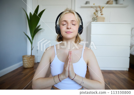 Wellbeing and people concept. Close up portrait of young woman in headphones, meditating, practice yoga, listens to podcast in earphones Wellbeing and people concept. Close up portrait of young woman in headphones, meditating, practice yoga, listens to podcast in earphones 113330800