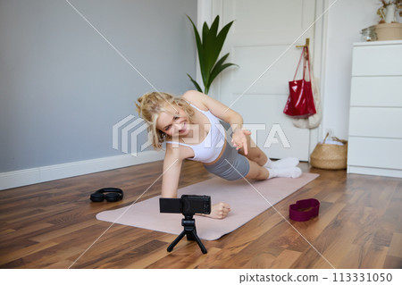 Portrait of fit and healthy young vlogger, fitness instructor woman standing in side plank, recording online lesson for clients on digital camera, shooting video about workout Portrait of fit and healthy young vlogger, fitness instructor woman standing in side plank, recording online lesson for clients on digital camera, shooting video about workout 113331050
