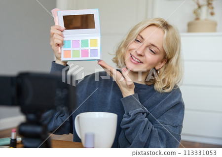 Portrait of beautiful lifestyle blogger, girl records a video on her camera for social media, shows palette of eyeshadows, does a makeup tutorial for her followers, sits in her room 113331053