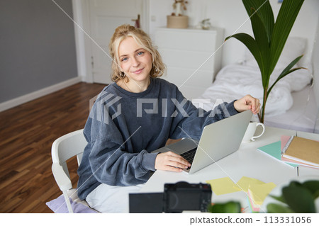 Portrait of young woman, lifestyle blogger, recording vlog video about her life and daily routine, sitting in front of laptop, talking to followers, sitting in her room Portrait of young woman, lifestyle blogger, recording vlog video about her life and daily routine, sitting in front of laptop, talking to followers, sitting in her room 113331056