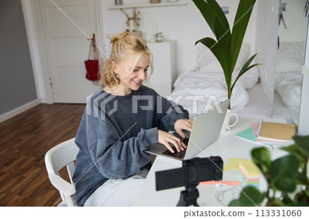 Portrait of woman sitting at desk with laptop, recording video of herself on laptop, making lifestyle video for social media account Portrait of woman sitting at desk with laptop, recording video of herself on laptop, making lifestyle video for social media account 113331060