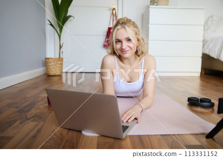 Portrait of young fitness woman, doing workout at home, looking at her gym instructor on laptop screen, doing online training session Portrait of young fitness woman, doing workout at home, looking at her gym instructor on laptop screen, doing online training session 113331152