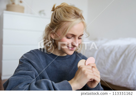 Image of young blond woman, girl records video about makeup, shows skin tone beauty products, sits in a room on floor 113331162
