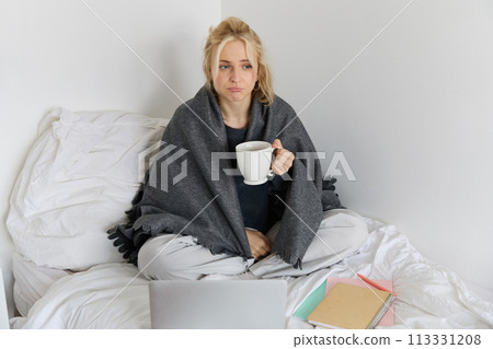 Portrait of woman catching a flu, sneezing, feeling sick, sitting on bed with laptop and working on remote while caught a cold 113331208