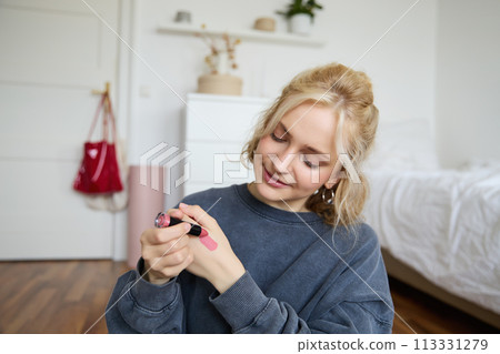 Portrait of young makeup artist, beauty blogger showing new lipstick, recording video in her room, smiling and expressing positivity 113331279