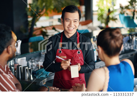 Smiling waiter talking to couple, recommending drinks and dishes of the day Smiling waiter talking to couple, recommending drinks and dishes of the day 113331337