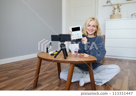 Portrait of beautiful smiling woman, recording video in her room, has camera on coffee table, reviewing makeup, doing lifestyle vlog for social media account, records a tutorial 113331447