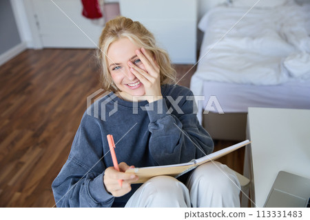 Portrait of smiling, charismatic young woman, writing down notes, making plans and putting it in planner, holding journal, sitting in bedroom and looking happy at camera Portrait of smiling, charismatic young woman, writing down notes, making plans and putting it in planner, holding journal, sitting in bedroom and looking happy at camera 113331483