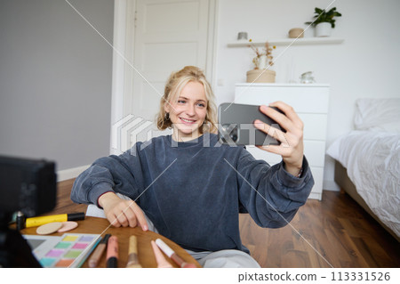 Portrait of young woman, girl beauty blogger, recording vlog in her bedroom, doing makeup tutorial for social media followers, taking selfies, live streaming on mobile phone app 113331526