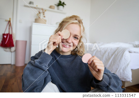 Portrait of young woman chatting on live stream about makeup, sits on floor in bedroom, showing beauty products to followers 113331547