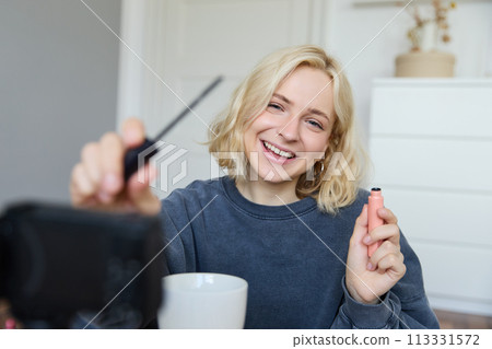 Image of cheerful, beautiful young lifestyle blogger, woman sitting on floor and recording video about makeup, holding mascara, making lifestyle content for her social media account and followers Image of cheerful, beautiful young lifestyle blogger, woman sitting on floor and recording video about makeup, holding mascara, making lifestyle content for her social media account and followers 113331572