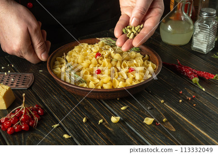 The chef adds aromatic spices to a plate of pasta. Working environment on the kitchen table of a public house. Delicious pasta with vegetables for lunch 113332049