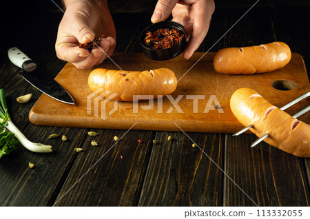 The chef adds dry spices with his hand to the Vienna sausages. Grill cooking concept with sausages and aromatic spices. Space for recipe or menu The chef adds dry spices with his hand to the Vienna sausages. Grill cooking concept with sausages and aromatic spices. Space for recipe or menu 113332055