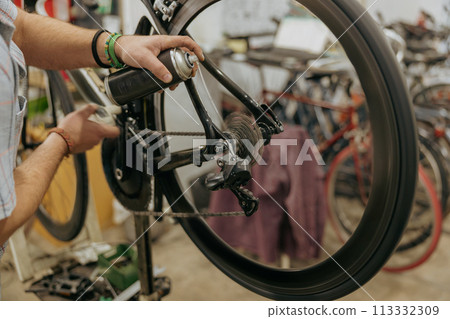 Close up of repairman is holding spray lubricant in his hand to lubricate the bike chain 113332309