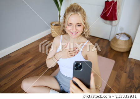 Portrait of young beautiful blond woman, fitness instructor doing exercises at home on yoga mat, taking selfies on smartphone, recording video of herself for social media account about workout Portrait of young beautiful blond woman, fitness instructor doing exercises at home on yoga mat, taking selfies on smartphone, recording video of herself for social media account about workout 113332931