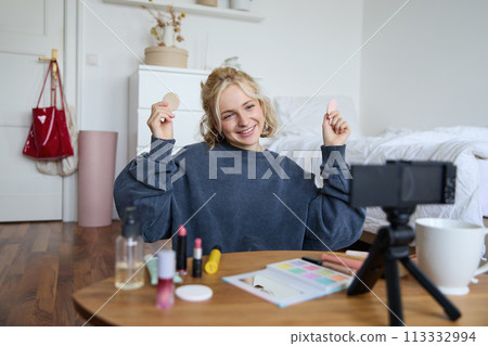 Portrait of beautiful and stylish young woman, vlogger recording video on her digital camera in a room, showing beauty products, making makeup tutorial for followers on social media Portrait of beautiful and stylish young woman, vlogger recording video on her digital camera in a room, showing beauty products, making makeup tutorial for followers on social media 113332994