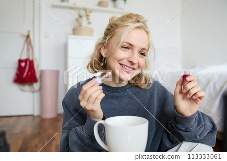 Portrait of smiling charismatic woman, puts on lip gloss, drinks tea, records video on digital camera, beauty content for social media account 113333061