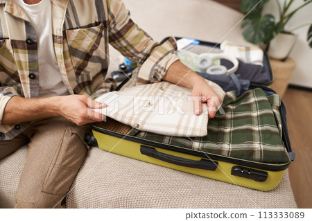 Cropped shot of male hands putting clothes inside suitcase, packing for business work trip or going on vacation, getting ready for holiday journey, preparing luggage Cropped shot of male hands putting clothes inside suitcase, packing for business work trip or going on vacation, getting ready for holiday journey, preparing luggage 113333089