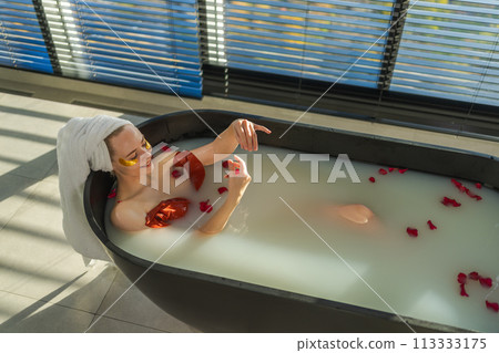 Spa relaxation. Woman lying in bath with red roses petals. Girl relaxing in bathroom at home. Pretty female enjoying taking hot bath. Stress relief. Rest after hard working day 113333175