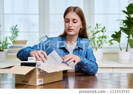 Satisfied young female shopper at home unpacks cardboard box with online purchases Satisfied young female shopper at home unpacks cardboard box with online purchases 113333541