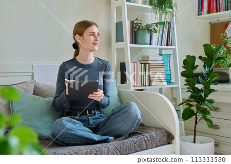 Young female teenager with digital tablet, stylus drawing illustrating sitting at home 113333580