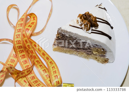 piece of a chocolate cake wrapped with a yellow measuring tape diet and healthy living concept image. piece of a chocolate cake wrapped with a yellow measuring tape diet and healthy living concept image. 113333786