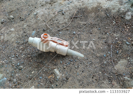 White Plastic Ball Valve With Water Pipe Sticking Out Of The Ground, Handle Is Red. Laid for watering plants and garden White Plastic Ball Valve With Water Pipe Sticking Out Of The Ground, Handle Is Red. Laid for watering plants and garden 113333927