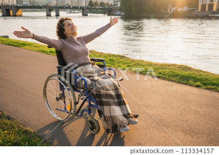 Happy senior woman in wheelchair raised hands enjoying freedom walking on road in city park outdoor. Old happy woman in chair for people with disability has a hope. Disability disease rehabilitation 113334157