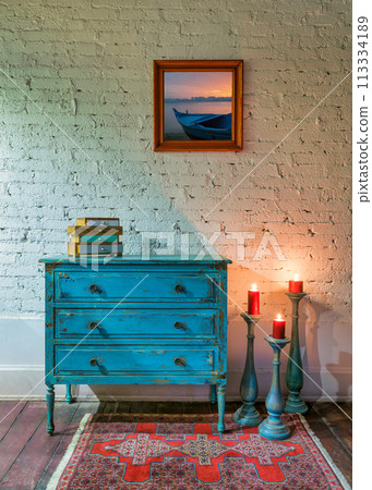Retro composition of Green vintage cabinet, candlesticks with lighted candles and hanged painting on white bricks wall Retro composition of Green vintage cabinet, candlesticks with lighted candles and hanged painting on white bricks wall 113334189