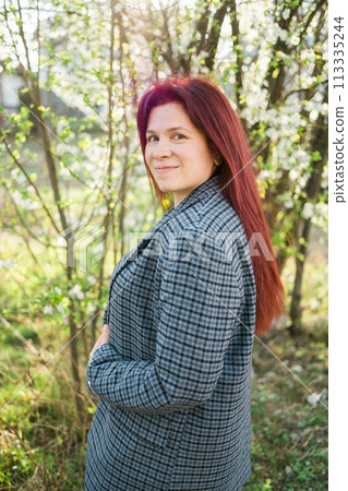 Beautiful young red hair woman near blooming spring trees alley. Youth and love, fashion and romantic and lifestyle concept. Beautiful young red hair woman near blooming spring trees alley. Youth and love, fashion and romantic and lifestyle concept. 113335244