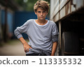 A young boy stands in front of a truck, wearing a gray shirt and black pants 113335332