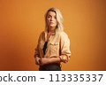 A blonde woman is wearing a tan shirt and black pants 113335337