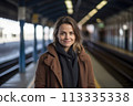 A woman wearing a brown coat and scarf stands in a train station 113335338
