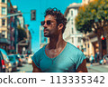 A man wearing a blue shirt and sunglasses stands on a city street 113335342