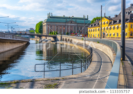 A serene view of Riddarholm Canal with the clear summer sky reflected in its waters, surrounded by historic buildings and a curving footpath. Stockholm, Sweden A serene view of Riddarholm Canal with the clear summer sky reflected in its waters, surrounded by historic buildings and a curving footpath. Stockholm, Sweden 113335757
