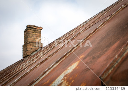 Old rusty metal roof with patches. Repair and renovation. Brick chimney Old rusty metal roof with patches. Repair and renovation. Brick chimney 113336489