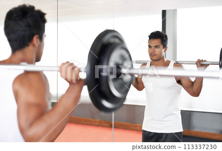 Man, barbell and weightlifting at mirror for training exercise as bodybuilder for workout strength, wellness or routine. Male person, equipment and reflection in Miami for healthy, biceps or sport 113337230