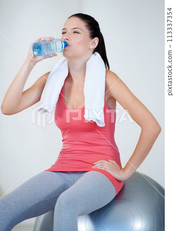 Ball, health or woman drinking water on break after exercise, workout or fitness training in gym. Thinking, tired lady or thirsty sports athlete with liquid bottle for wellness, resting or hydration 113337354