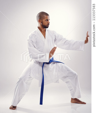 Studio, karate and black man with martial arts, training and blue belt for instructor in white background. Discipline, male person and adult with technique for health, goju ryu and movement for power 113337383